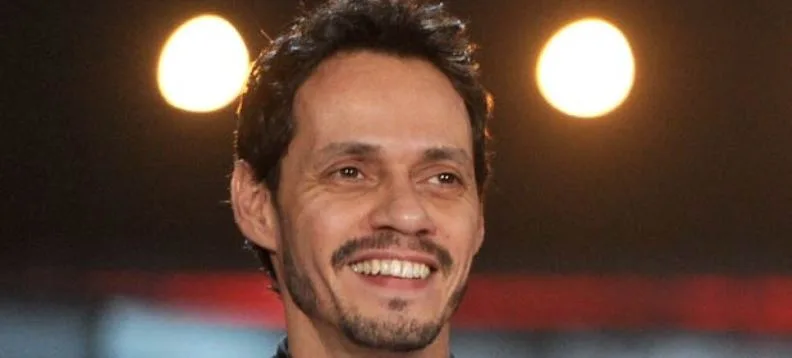 Ο Marc Anthony χαμογελάει μπροστά από φωτισμένο φόντο.