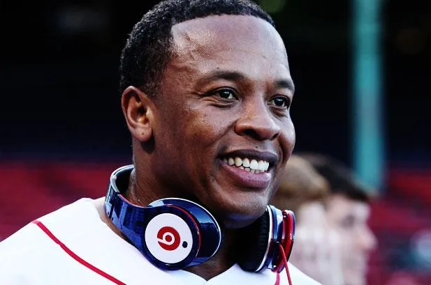 Ο Dr. Dre χαμογελάει φορώντας ακουστικά Beats γύρω από τον λαιμό του.