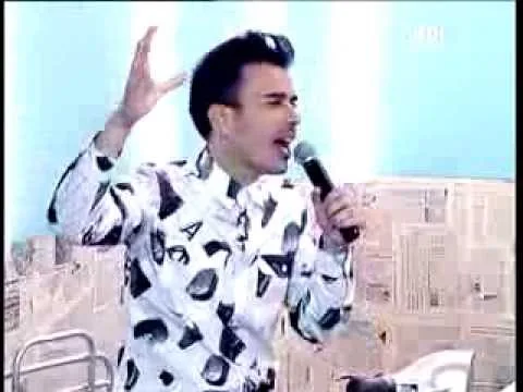 Ο Σταμάτης Γονίδης τραγουδάει με μικρόφωνο σε τηλεοπτικό πλατό.