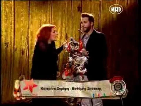 Η Κατερίνα Ζαρίφη και ο Ευθύμης Ζησάκης σε τηλεοπτικό πλατό με εορταστική διακόσμηση.