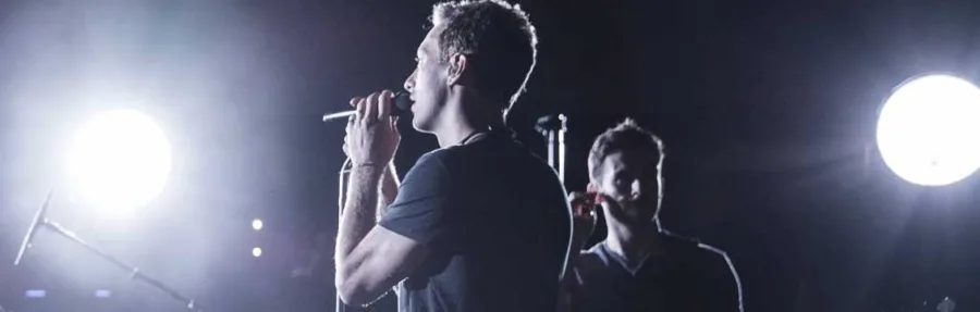 Ο Chris Martin των Coldplay τραγουδάει σε σκηνή με έντονο φωτισμό.