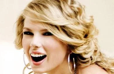 Η Taylor Swift χαμογελάει με ξανθά σγουρά μαλλιά και μεγάλους κρίκους.