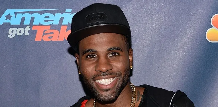 Ο Jason Derulo χαμογελάει μπροστά από το λογότυπο του America's Got Talent.