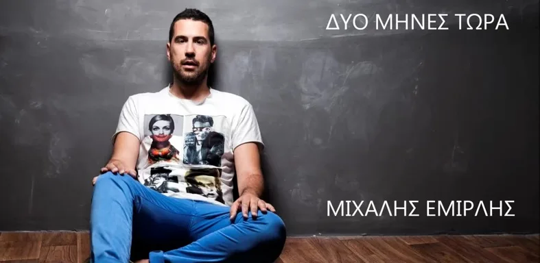 Ο Μιχάλης Εμιρλής κάθεται στο πάτωμα μπροστά από έναν γκρίζο τοίχο.