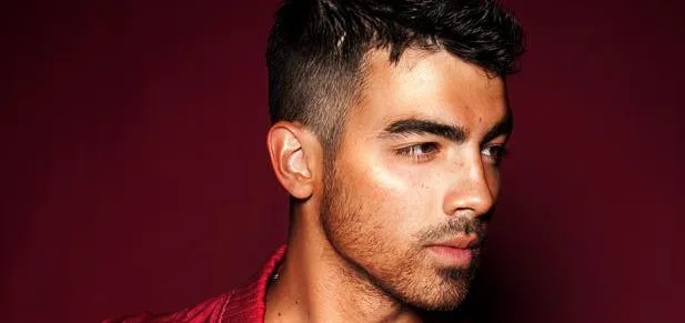 Κοντινό πορτρέτο του Joe Jonas με κόκκινο φόντο.