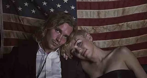 Η Miley Cyrus και ένας άνδρας μπροστά από την αμερικανική σημαία.
