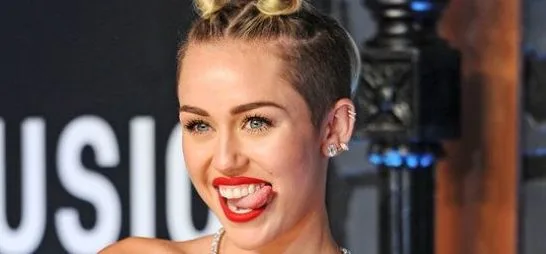 Η Miley Cyrus με ξυρισμένο κεφάλι και κόκκινο κραγιόν βγάζει τη γλώσσα της.