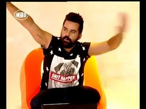 Παρουσιαστής με μαύρο t-shirt με στάμπα σκύλου και αστέρια σε πορτοκαλί κάθισμα.