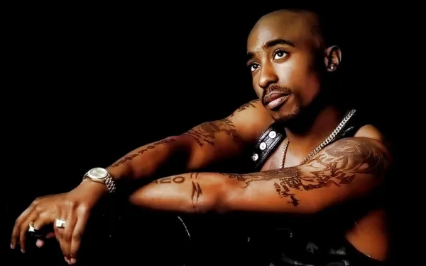 Ο 2Pac ποζάρει με τατουάζ και κοσμήματα σε μαύρο φόντο.