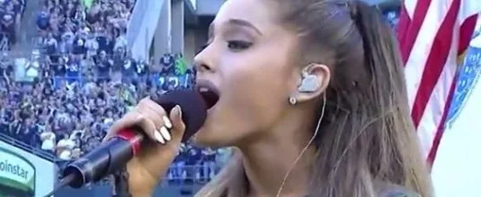Η Ariana Grande τραγουδάει σε μικρόφωνο σε στάδιο.