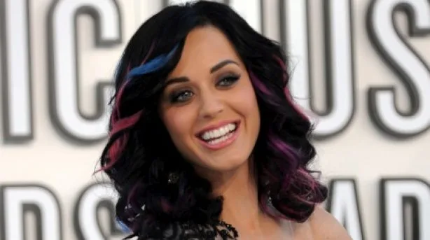 Η Katy Perry χαμογελάει σε εκδήλωση με μαύρα σπαστά μαλλιά και χρωματιστές ανταύγειες.