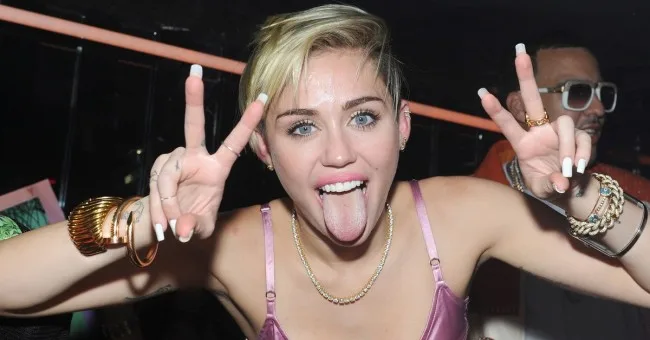 Η Miley Cyrus κάνει το σήμα της ειρήνης με τη γλώσσα έξω.