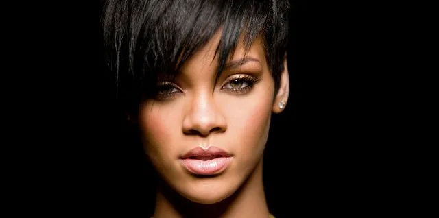 Κοντινό πορτρέτο της Rihanna με κοντό μαύρο κούρεμα σε μαύρο φόντο.