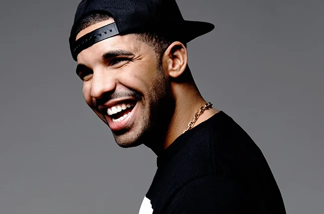 Ο Drake χαμογελάει φορώντας μαύρο καπέλο και μαύρο t-shirt.
