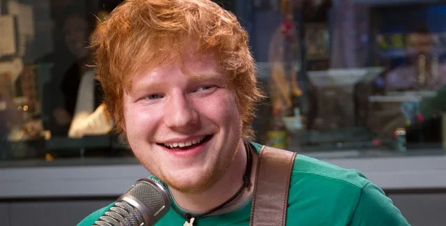 Ο Ed Sheeran χαμογελάει μπροστά σε ένα μικρόφωνο.