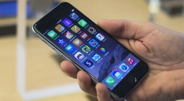 Ένα iPhone 6 στο χέρι ενός χρήστη που δείχνει την αρχική οθόνη με διάφορες εφαρμογές.