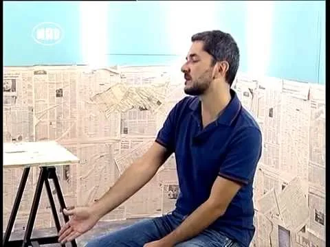Ο Λουκάς Κατσίκας σε τηλεοπτικό στούντιο με φόντο εφημερίδες.