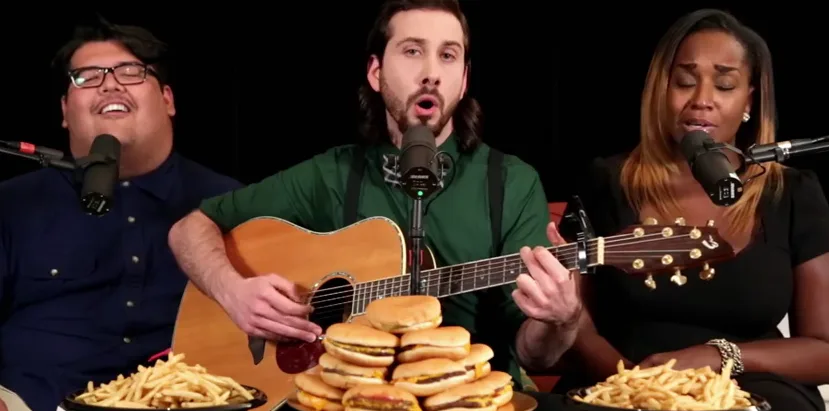 Ο Avi Kaplan με μέλη των Pentatonix τραγουδούν μπροστά από μια στοίβα χάμπουργκερ.