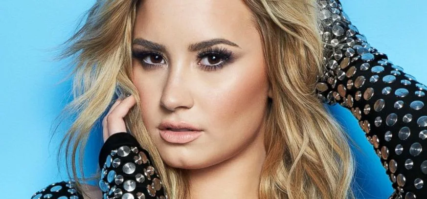 Η Demi Lovato ποζάρει με ξανθά μαλλιά και μαύρο ρούχο με μεταλλικά τρουκς.