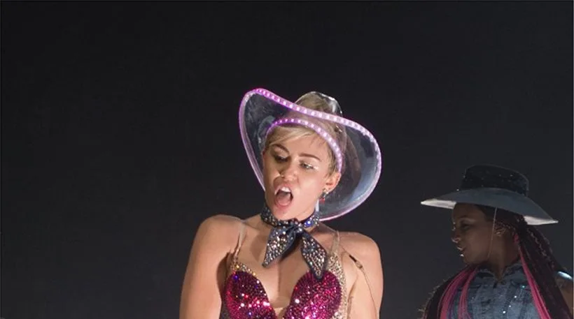 Η Miley Cyrus στη σκηνή με διάφανο καουμπόικο καπέλο και λαμπερό μπούστο.