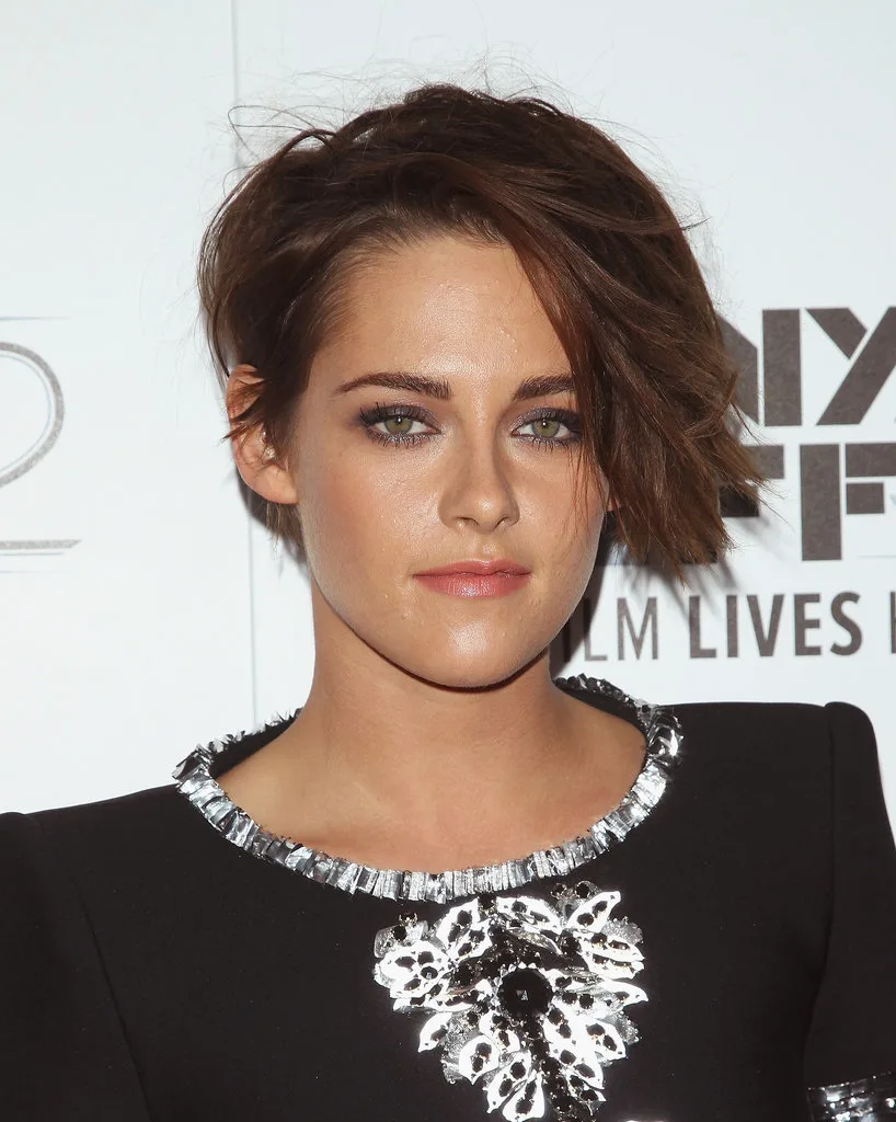 Η Kristen Stewart με κοντό καστανό κούρεμα και μαύρο φόρεμα με κεντημένες λεπτομέρειες.
