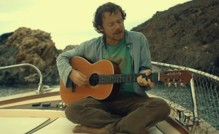 Ο Damien Rice παίζει ακουστική κιθάρα καθισμένος σε ένα σκάφος.