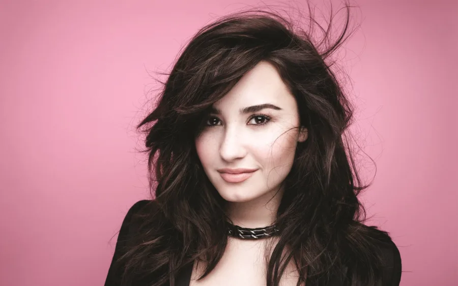 Κοντινό πορτρέτο της Demi Lovato με σκούρα μαλλιά σε ροζ φόντο.