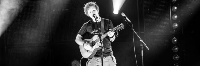 Ο Ed Sheeran τραγουδάει και παίζει κιθάρα σε συναυλία.