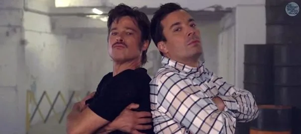 Ο Brad Pitt και ο Jimmy Fallon ποζάρουν πλάτη-πλάτη με σταυρωμένα χέρια.