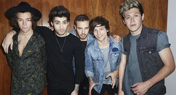 Το συγκρότημα One Direction ποζάρει μπροστά από ξύλινο τοίχο.