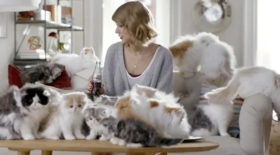 Η Taylor Swift περιτριγυρισμένη από πολλές γάτες σε καναπέ.