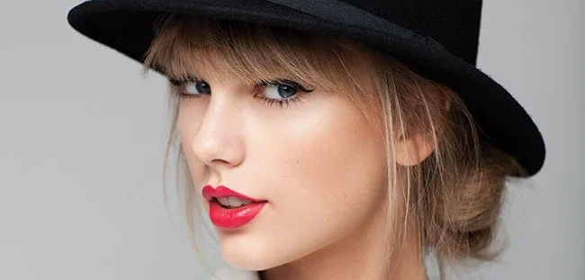 Κοντινό πορτρέτο της Taylor Swift με μαύρο καπέλο και κόκκινο κραγιόν.