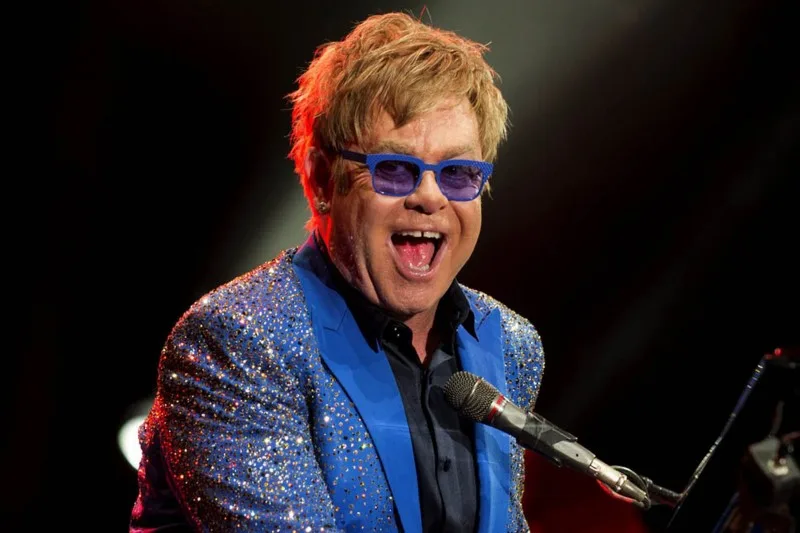 Ο Sir Elton John στη σκηνή με μπλε σακάκι και γυαλιά.