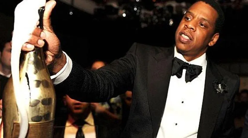 Ο Jay-Z κρατάει ένα μπουκάλι σαμπάνιας που αφρίζει.