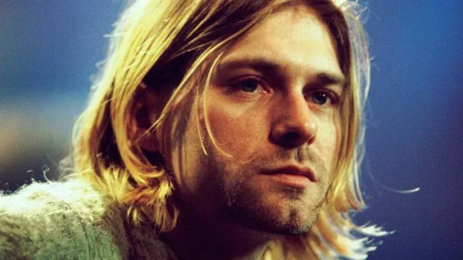 Κοντινό πλάνο του Kurt Cobain με ξανθά μαλλιά και γκρι πουλόβερ.