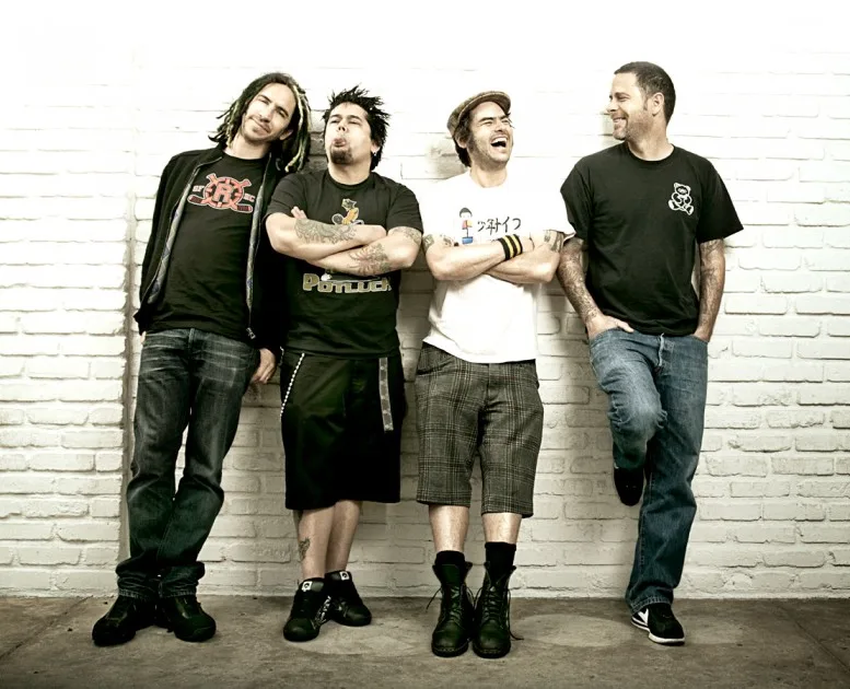 Το punk-rock συγκρότημα NOFX ποζάρει μπροστά από έναν λευκό τοίχο με τούβλα.