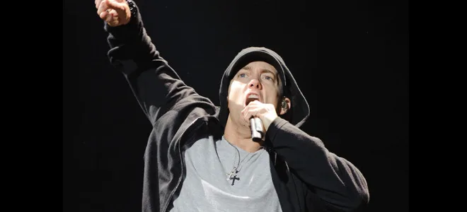 Ο Eminem στη σκηνή με μαύρη ζακέτα και κουκούλα κρατώντας μικρόφωνο.
