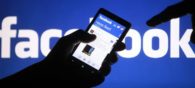 Χρήση του Facebook σε smartphone με φόντο το λογότυπο της εταιρείας