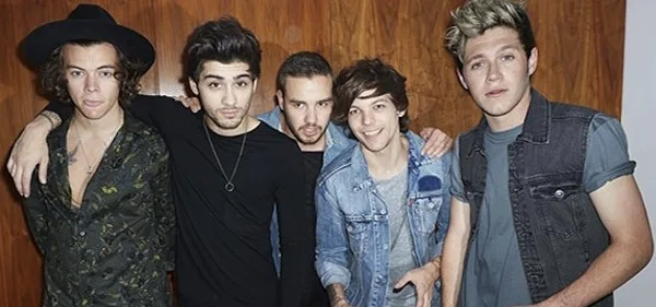 Το συγκρότημα One Direction ποζάρει μπροστά από ξύλινο τοίχο.
