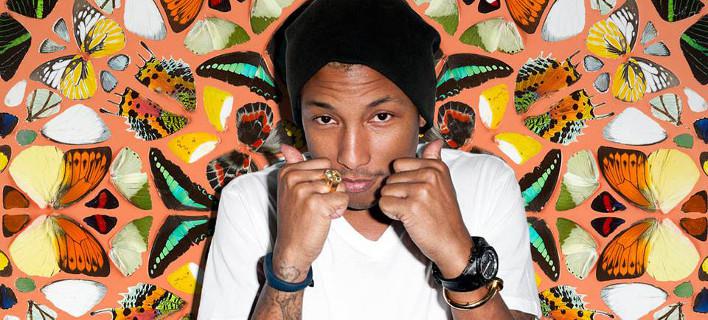 Ο Pharrell Williams με μαύρο σκούφο και λευκό t-shirt μπροστά από φόντο με πεταλούδες.