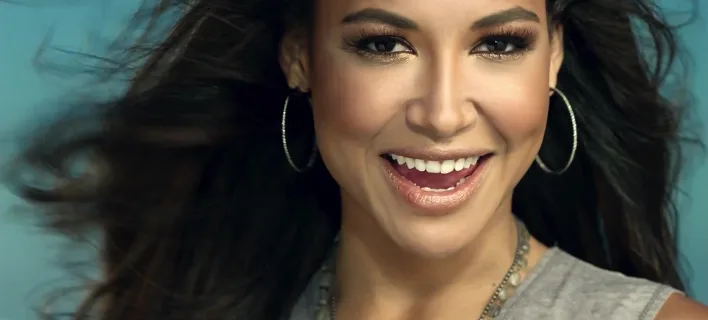 Η Naya Rivera χαμογελάει με φόντο γαλάζιο χρώμα.