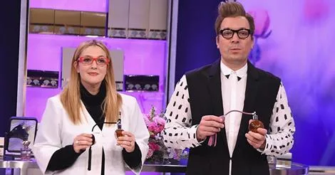 Η Drew Barrymore και ο Jimmy Fallon σε τηλεοπτικό πλατό κρατώντας μπουκάλια αρώματος.