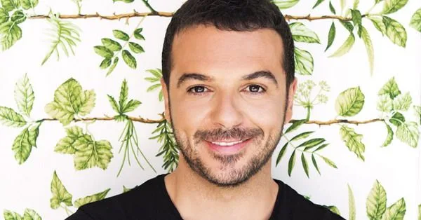 Ο Τριαντάφυλλος χαμογελά μπροστά από φόντο με πράσινα φύλλα.