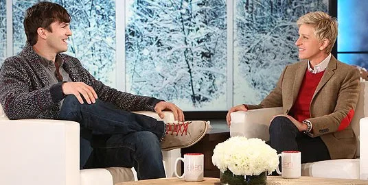Ο Ashton Kutcher και η Ellen DeGeneres σε τηλεοπτικό πλατό με χειμερινό φόντο.