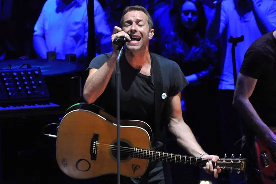 Ο Chris Martin των Coldplay τραγουδάει παίζοντας ακουστική κιθάρα σε συναυλία.