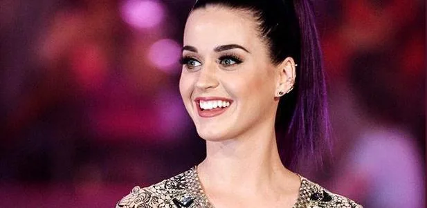 Η Katy Perry χαμογελάει με μωβ μαλλιά πιασμένα αλογοουρά.