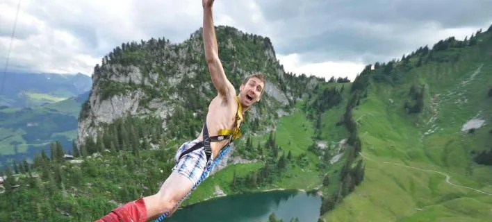 Άνδρας κάνει bungee jumping πάνω από λίμνη και βουνά.