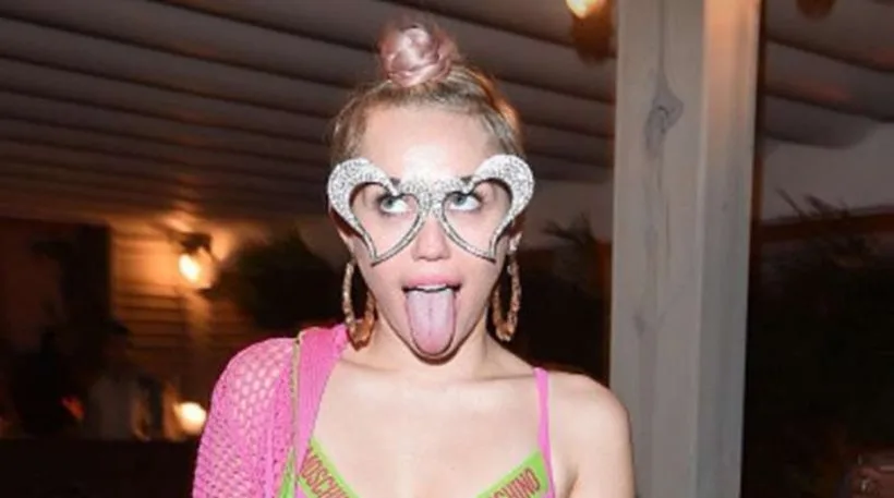 Η Miley Cyrus με γυαλιά σε σχήμα καρδιάς και ροζ ρούχα.