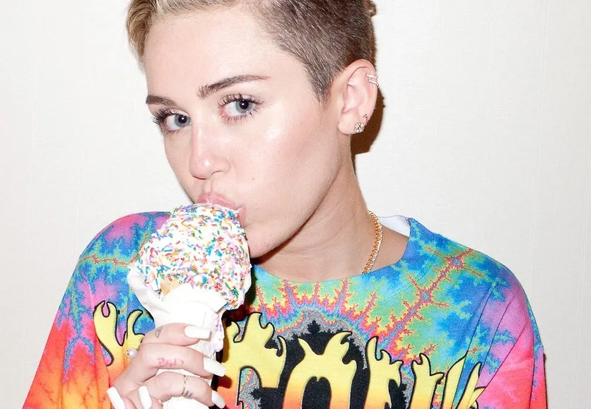 Η Miley Cyrus με κοντό ξανθό μαλλί τρώει παγωτό χωνάκι με πολύχρωμη τρούφα.