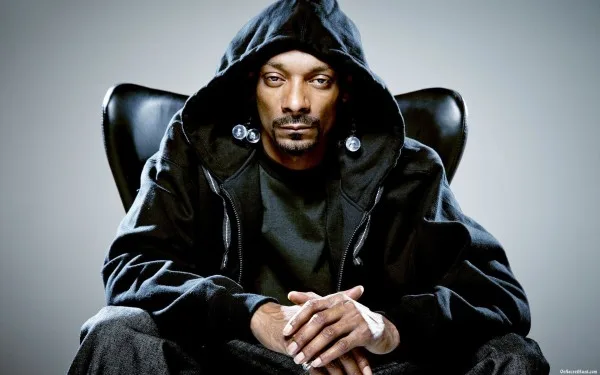 Ο Snoop Dogg με μαύρη ζακέτα με κουκούλα κάθεται σε δερμάτινη πολυθρόνα.